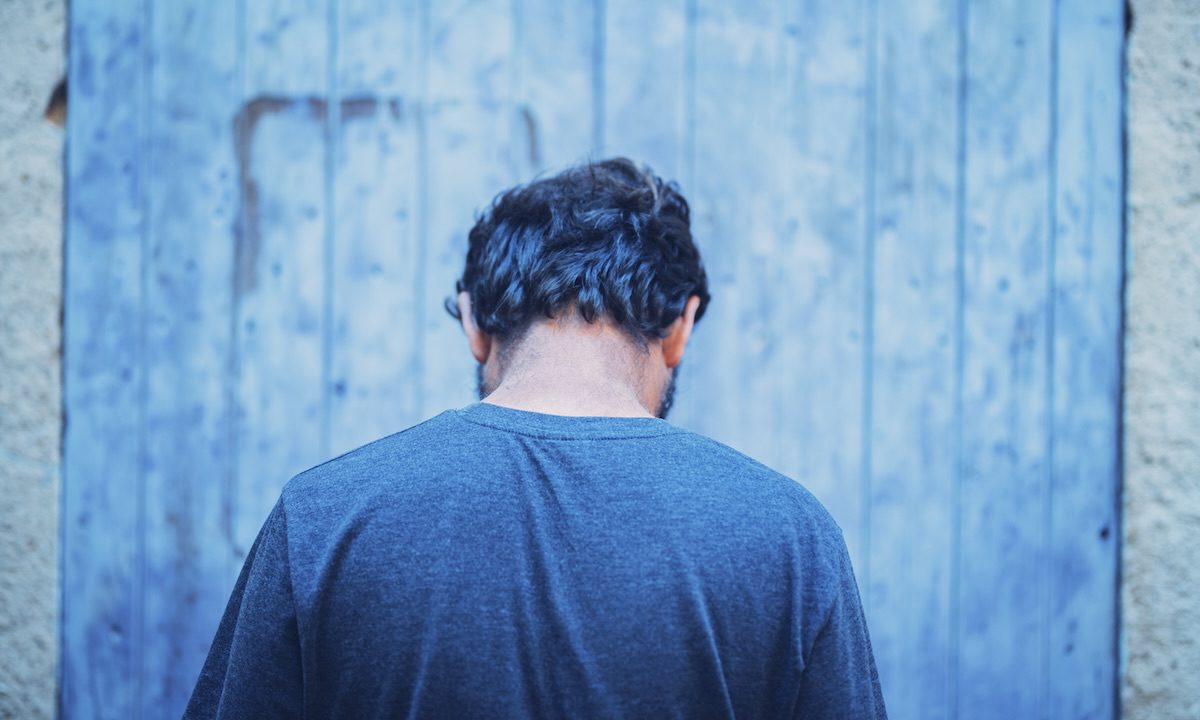 Man turning back to camera feeling alone. Rear view of thoughtful man feeling lonely or sad. Back of displeased man in deep thought with face down in negative emotion