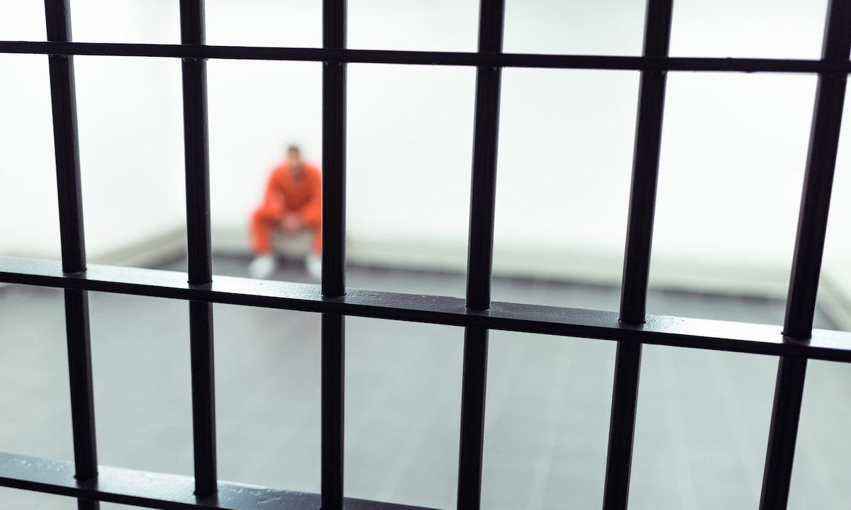 prisoner sitting on bench with prison bars on foreground