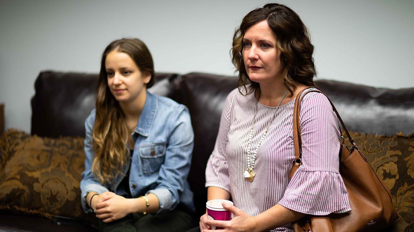 there are two women sitting on a couch with a cup of coffee