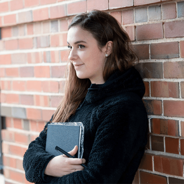 arafed woman leaning against a brick wall with a book