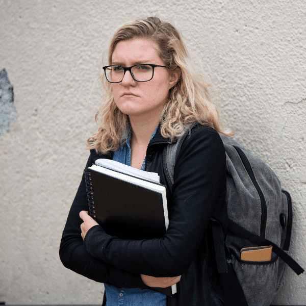 blond woman with glasses and a backpack holding a book