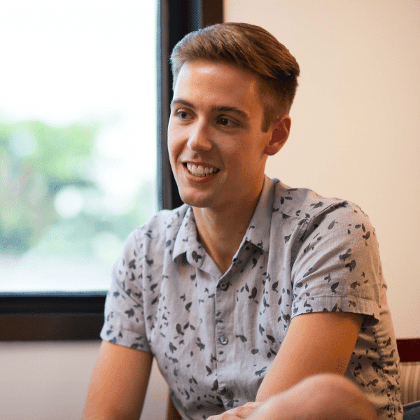 there is a man sitting in front of a window with a remote