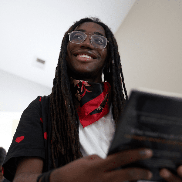 smiling man with dreadlocks and glasses holding a laptop computer