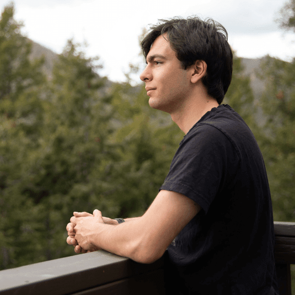 arafed man sitting on a balcony looking out over a forest