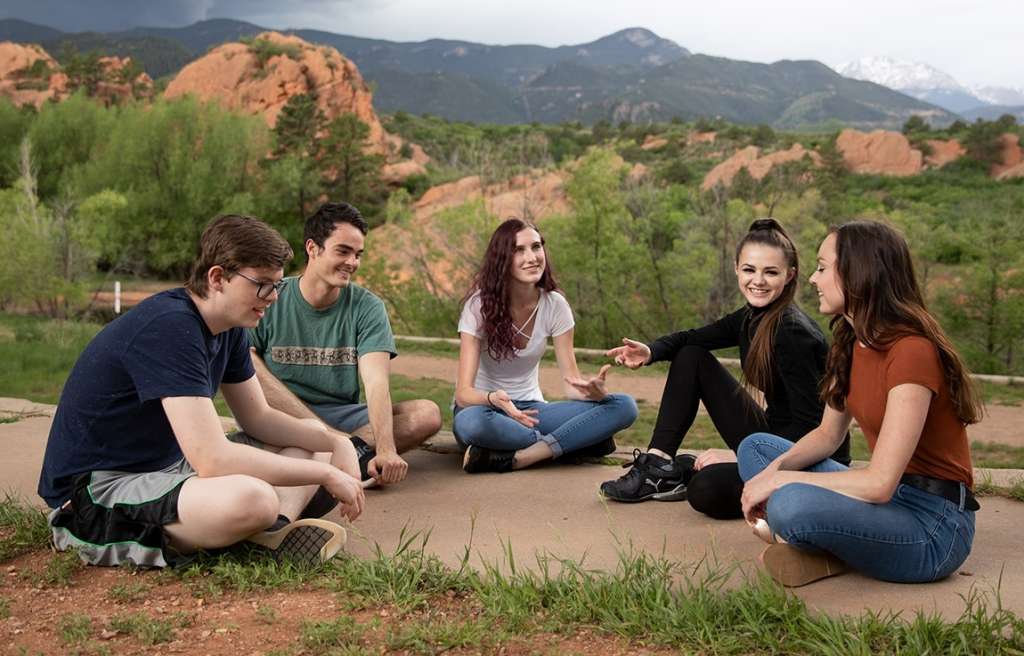 Group therapy discussion between several teens sitting outdoors at Colorado teen rehab in Cascade Canyon.