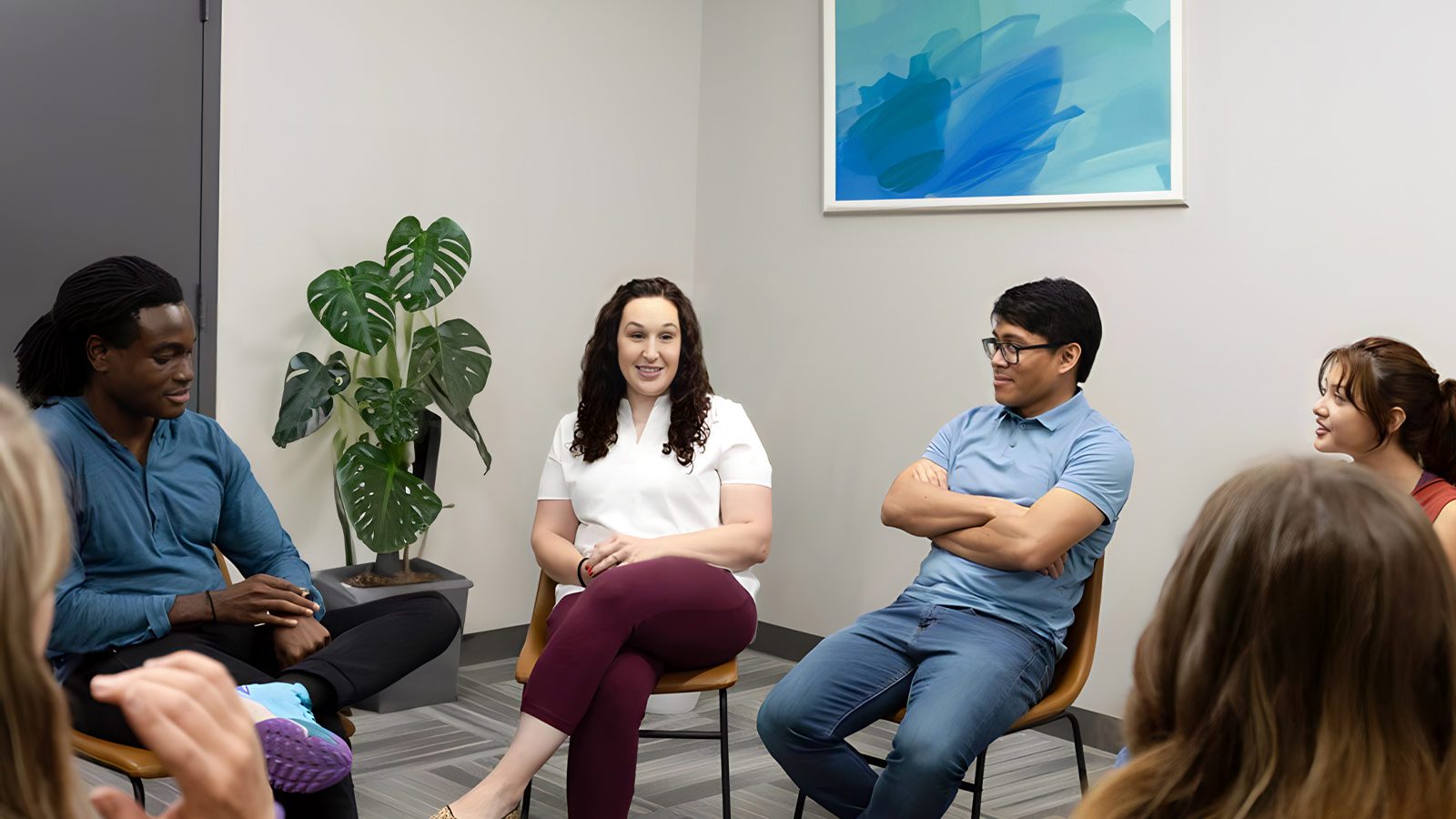 several people sitting in a circle in a room with a plant