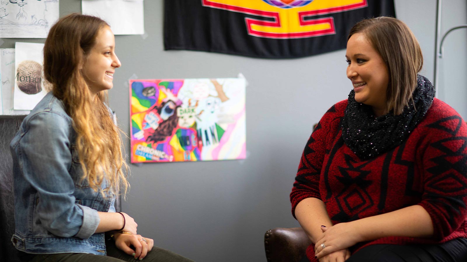 two women sitting in chairs talking to each other in a room