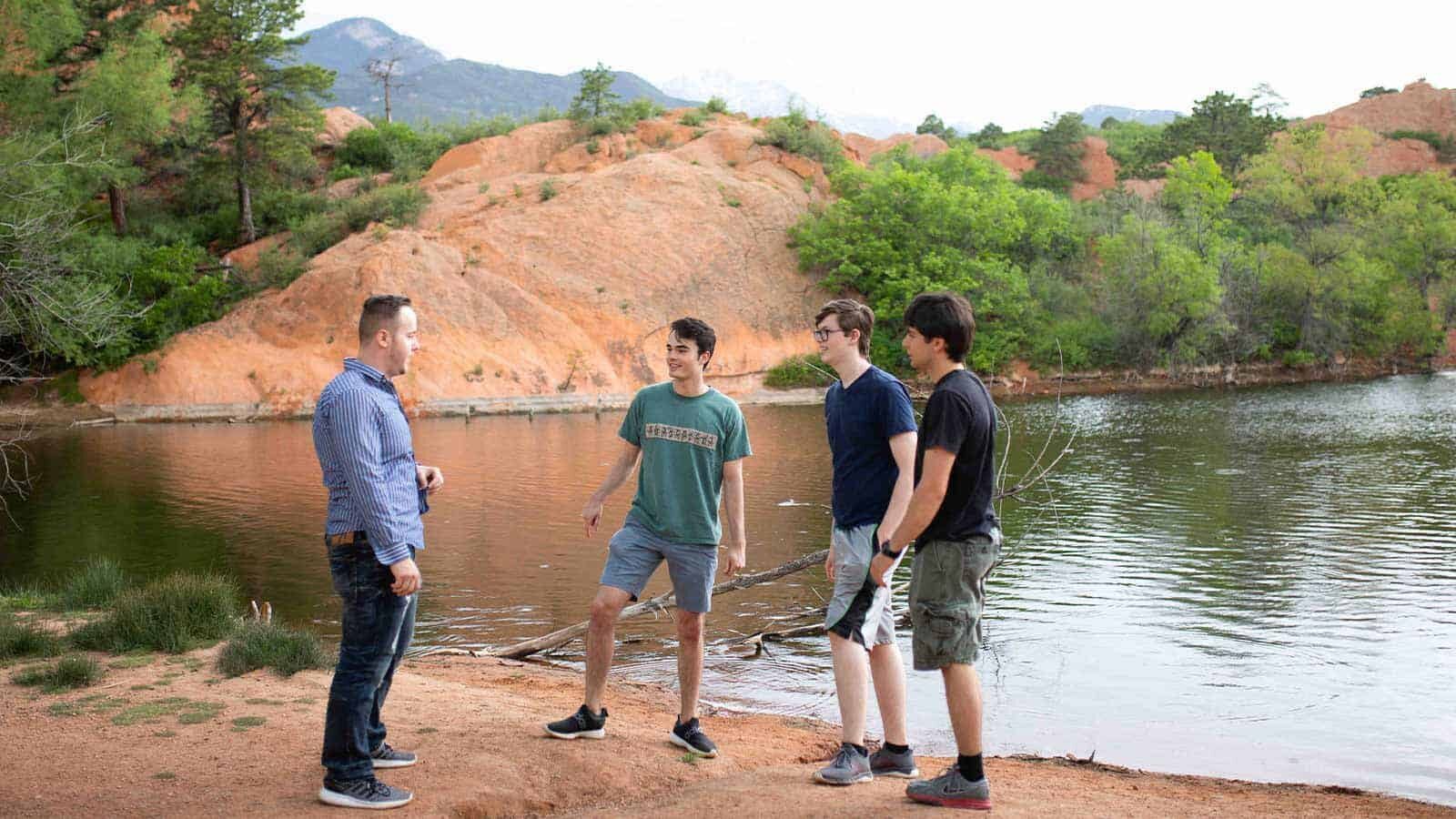 Three teenage boys standing on a beach of a lake in Cascade talking to their counselor.