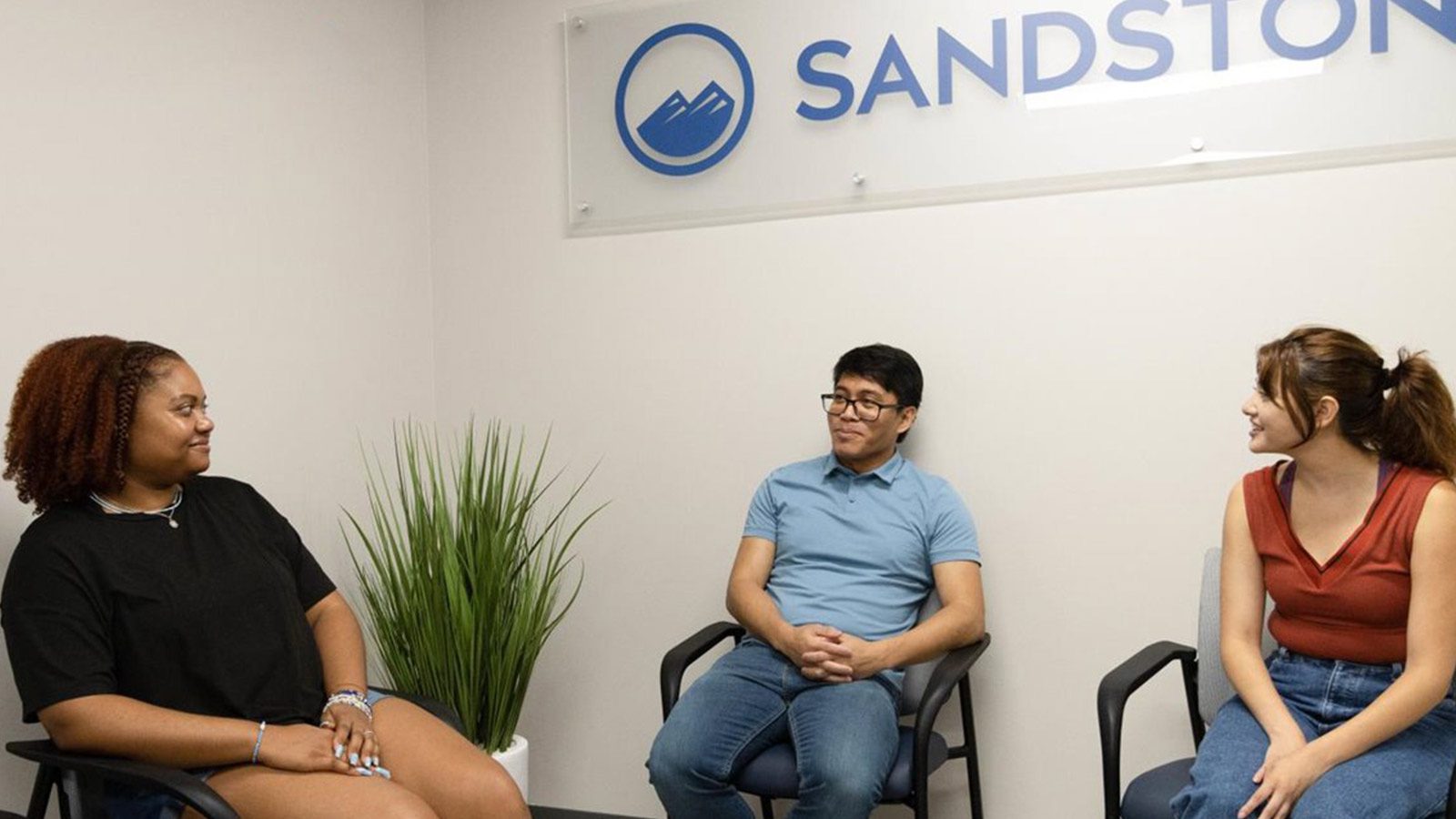 three people sitting in chairs in a room with a sign that says sandstone
