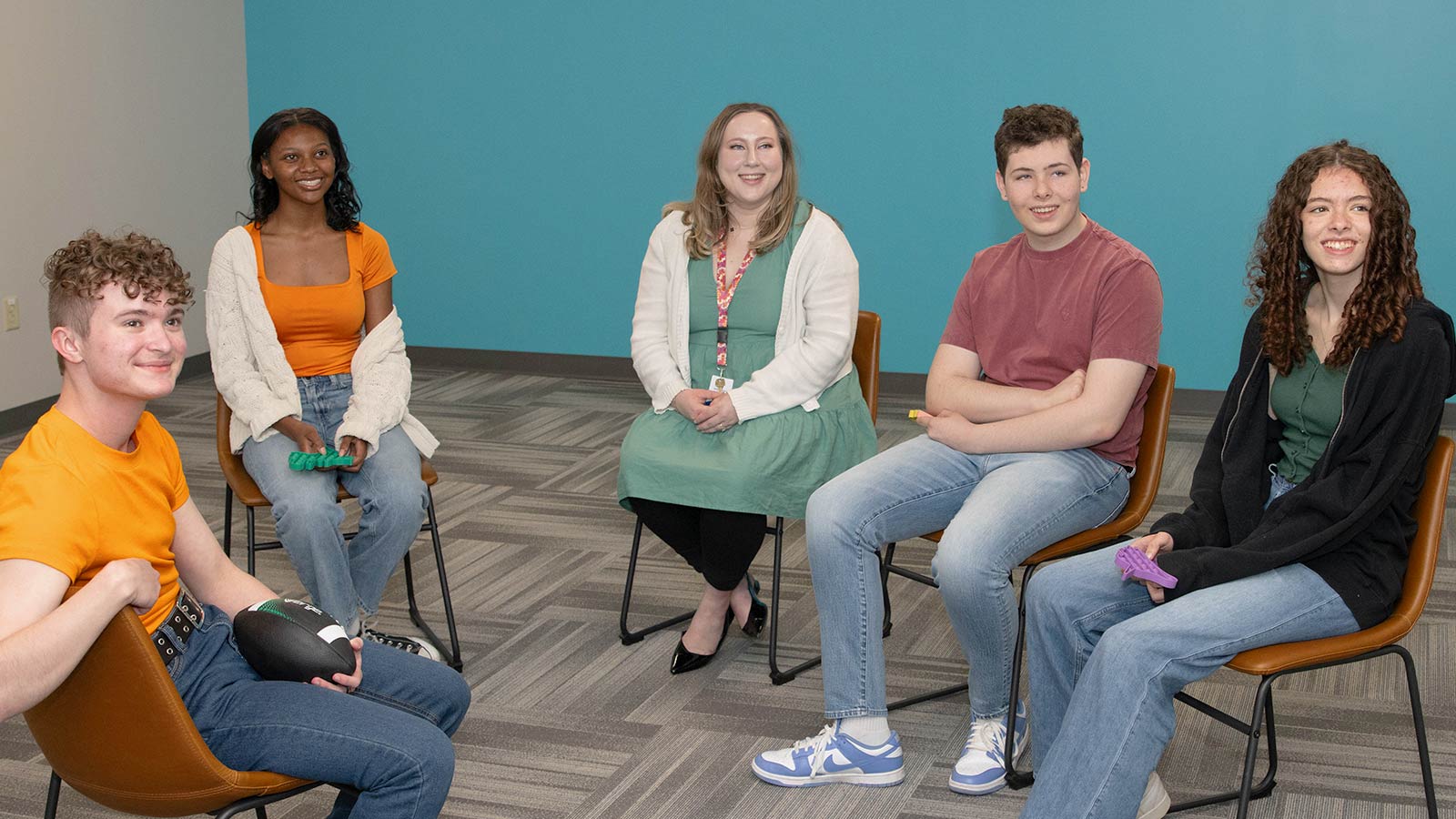 Several teens sitting in chairs in a room with a blue wall.