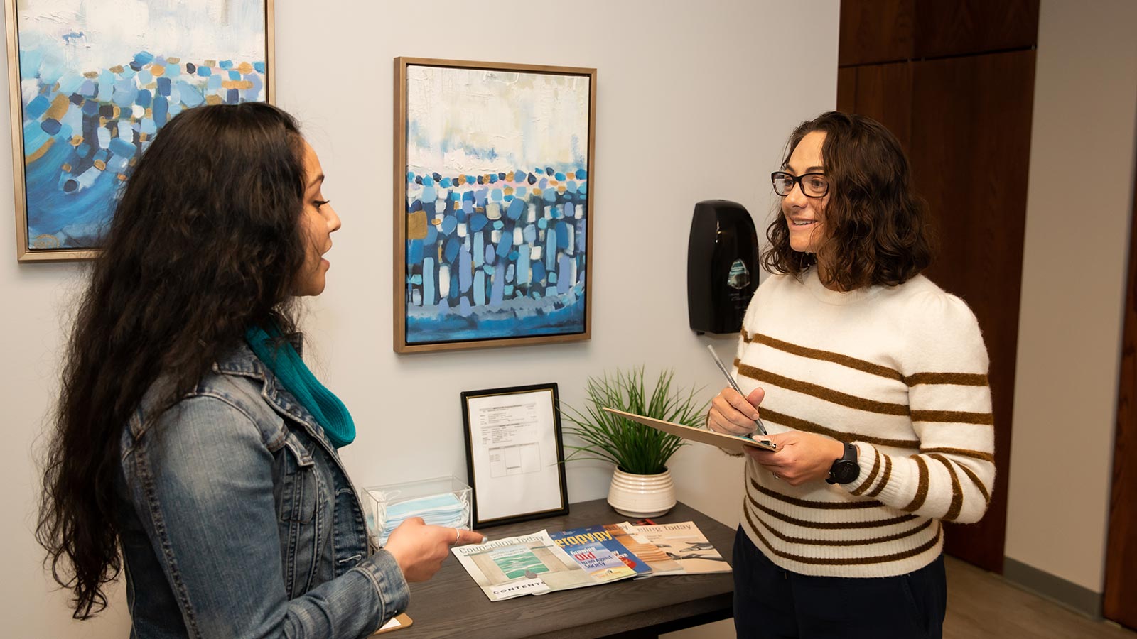 two women standing in a room with paintings on the wall