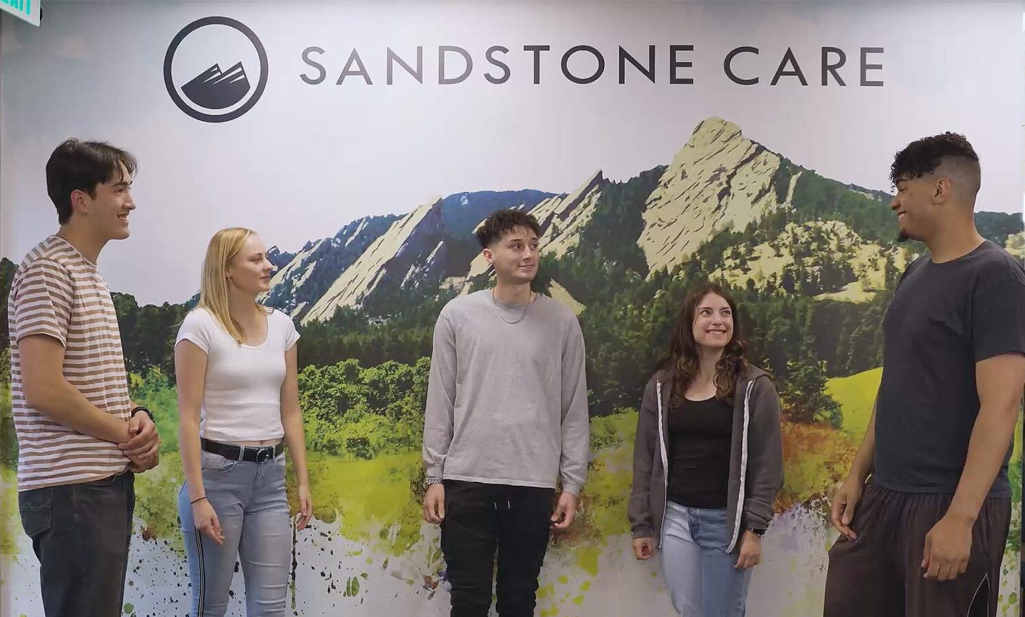 A group of young adults standing in front of a sign with a mountain backdrop
