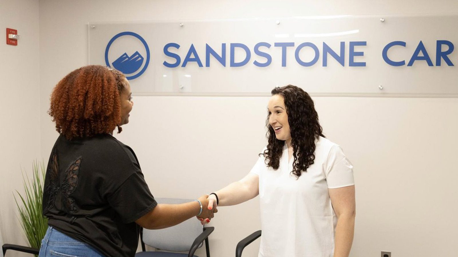 A woman shaking hands with a woman in a white shirt