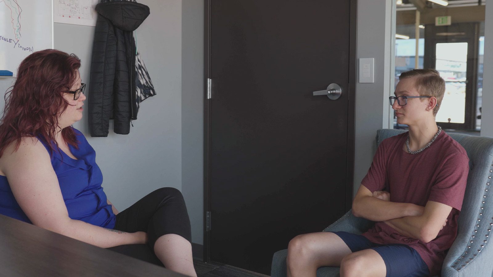 A female therapist and young man sitting in chairs talking at the Mental Health Colorado Springs center