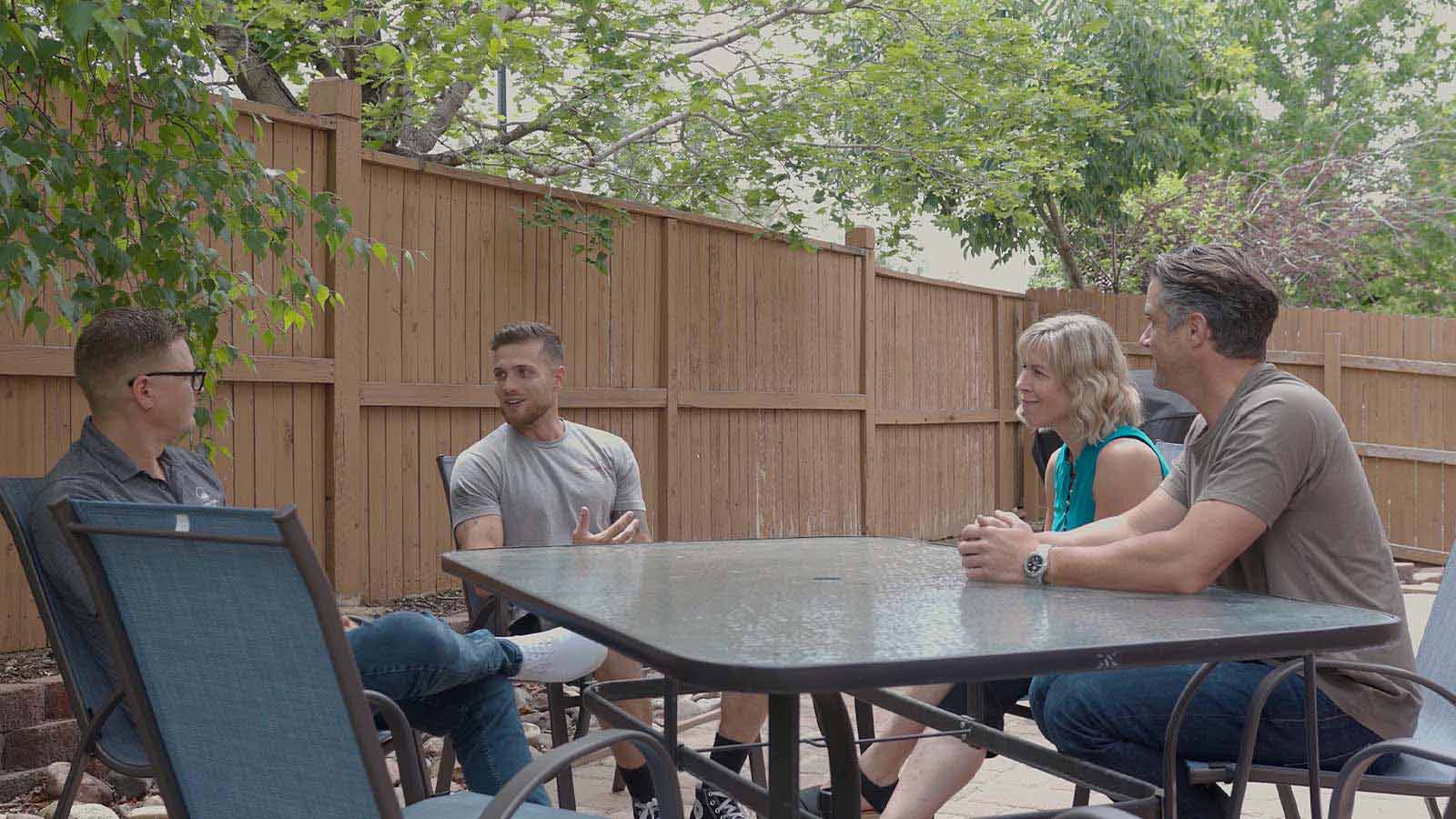 several people sitting around a table outside in a backyard