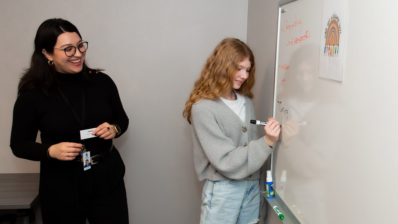 there are two women standing in front of a whiteboard with writing on it