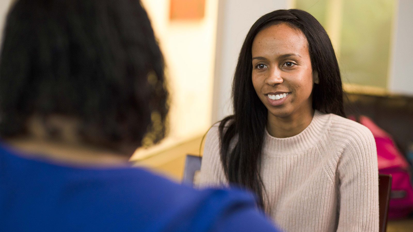 smiling woman sitting in a chair talking to another woman