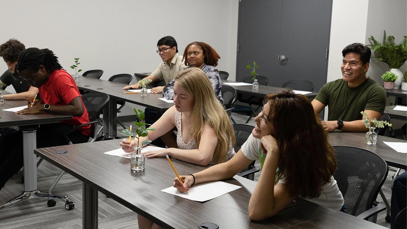 several people sitting at tables in a classroom with papers and pens