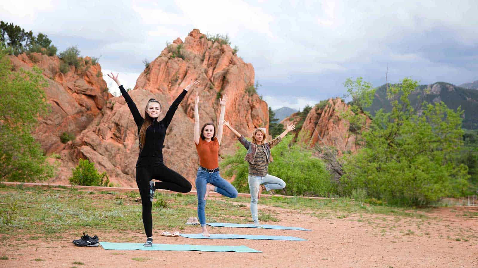 Three teenagers stand in a yoga pose in front of mountains and greenery in Cascade, Colorado.