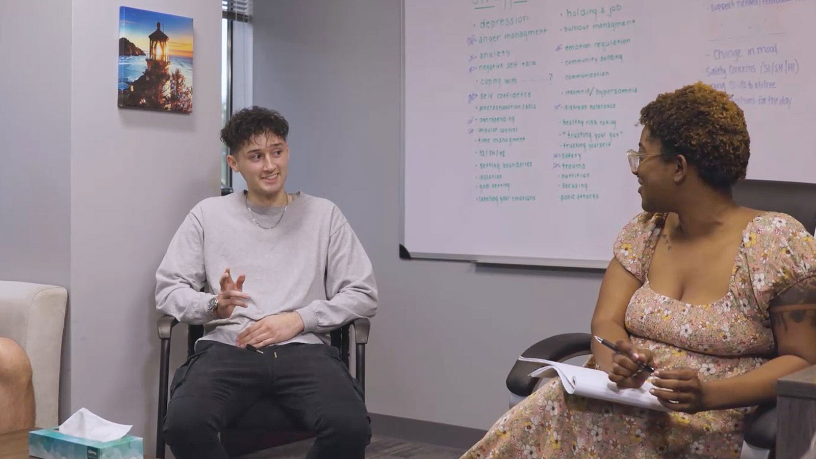 several people sitting in chairs talking in a room with a whiteboard
