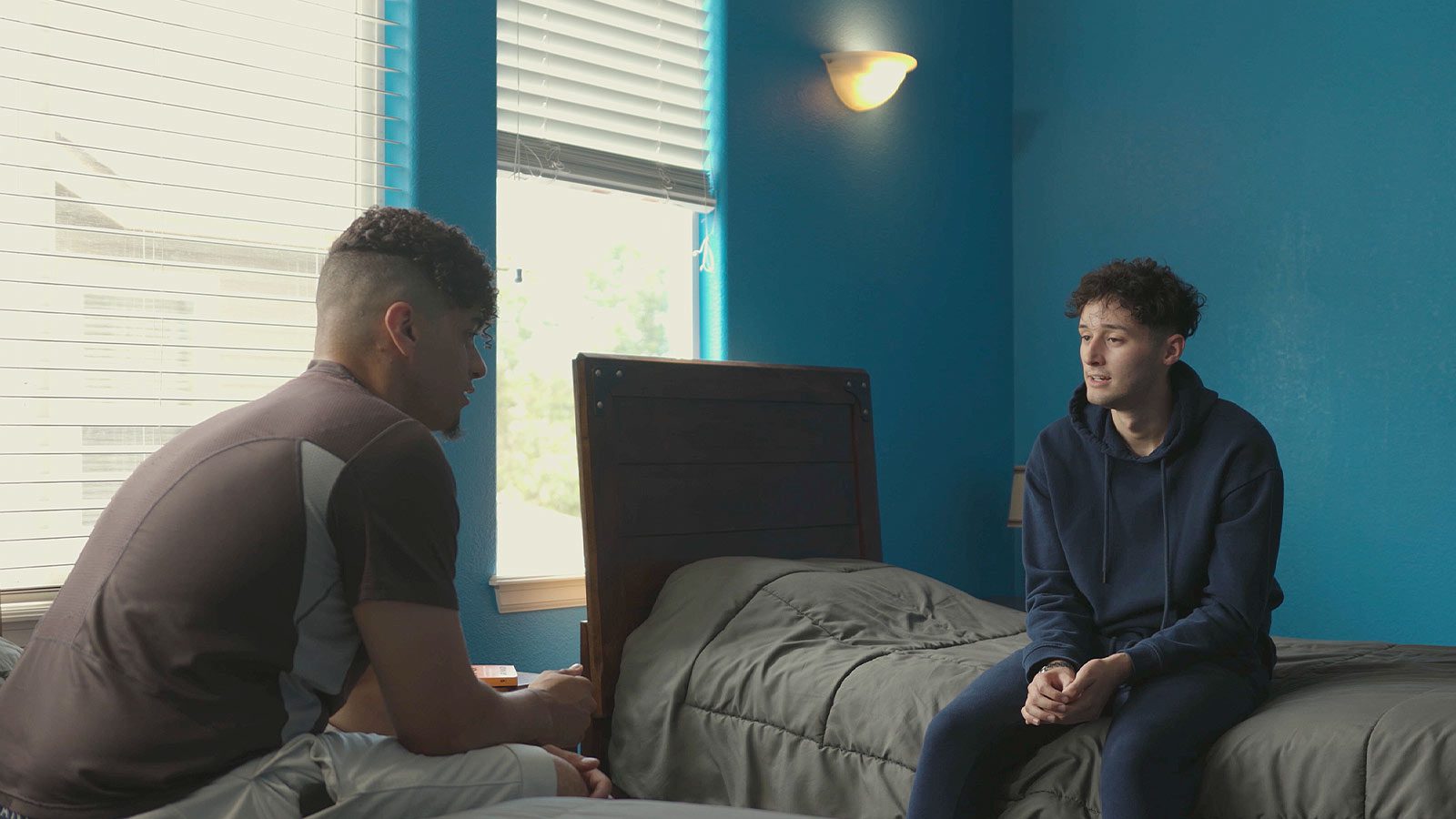 there are two men sitting on a bed talking to each other