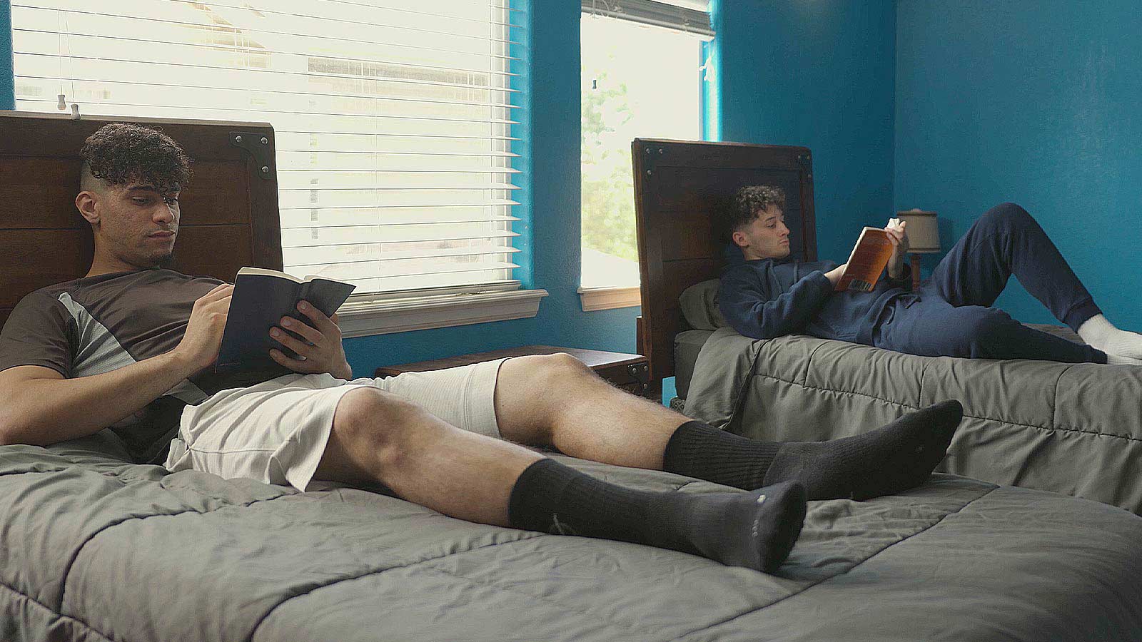 there are two men sitting on a bed reading books