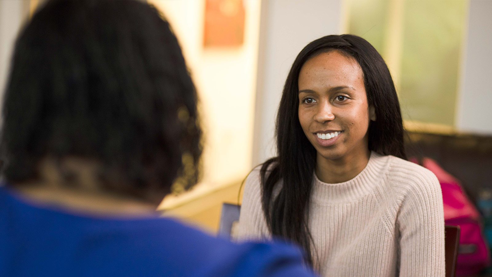 smiling woman in a blue sweater talking to another woman in a room