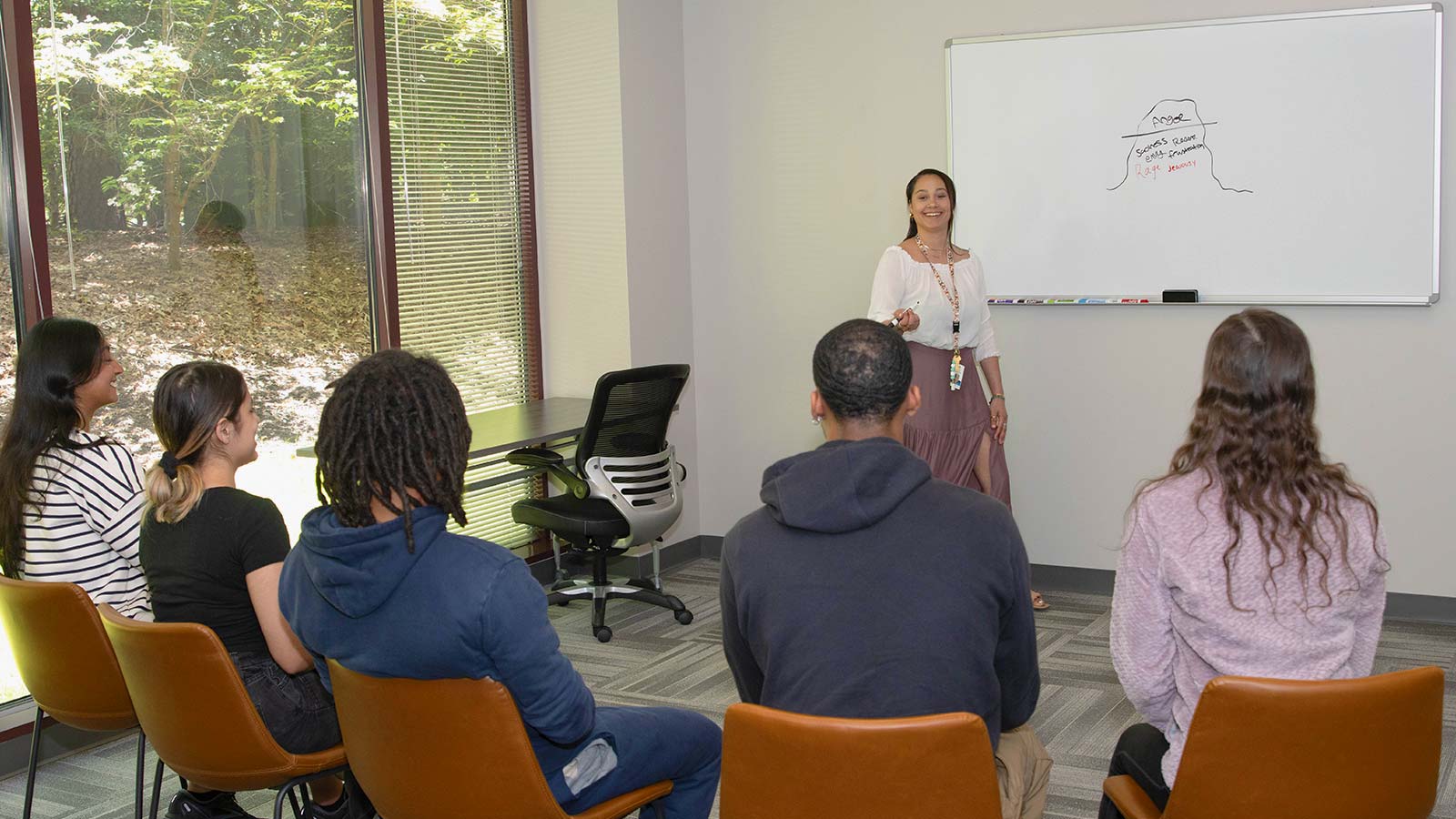 A group of young adults pay attention to a teaching standing in front of a whiteboard.