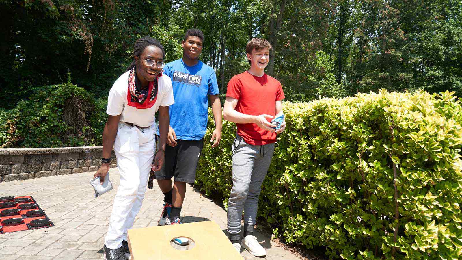 three young men standing next to each other near a hedge