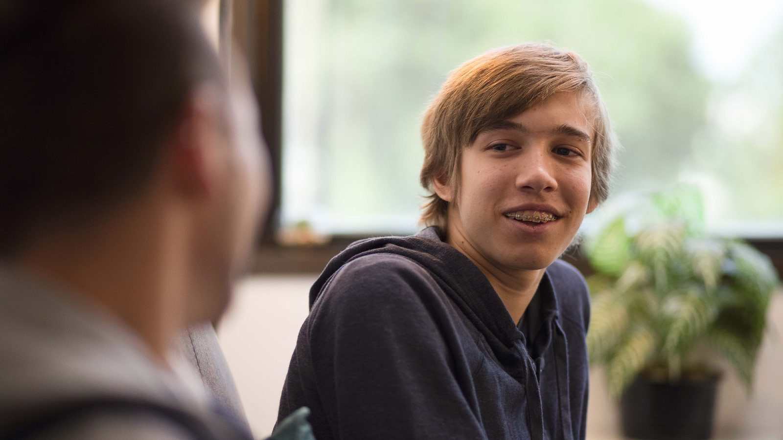 there is a man sitting at a table with a plant in the background