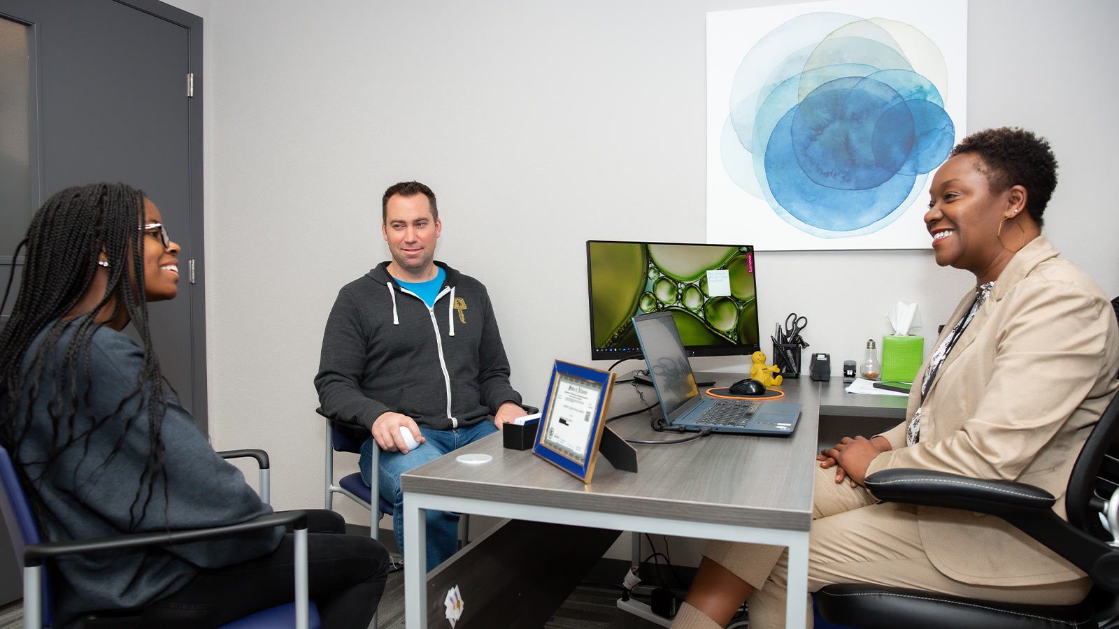 there are three people sitting at a table with laptops