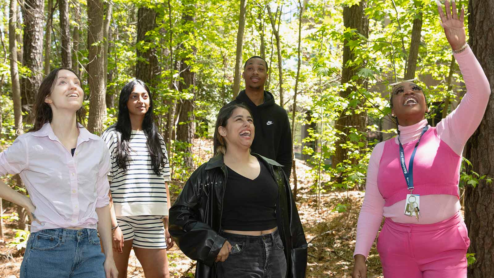 A program director leads a group of young adults through the woods on a hike.