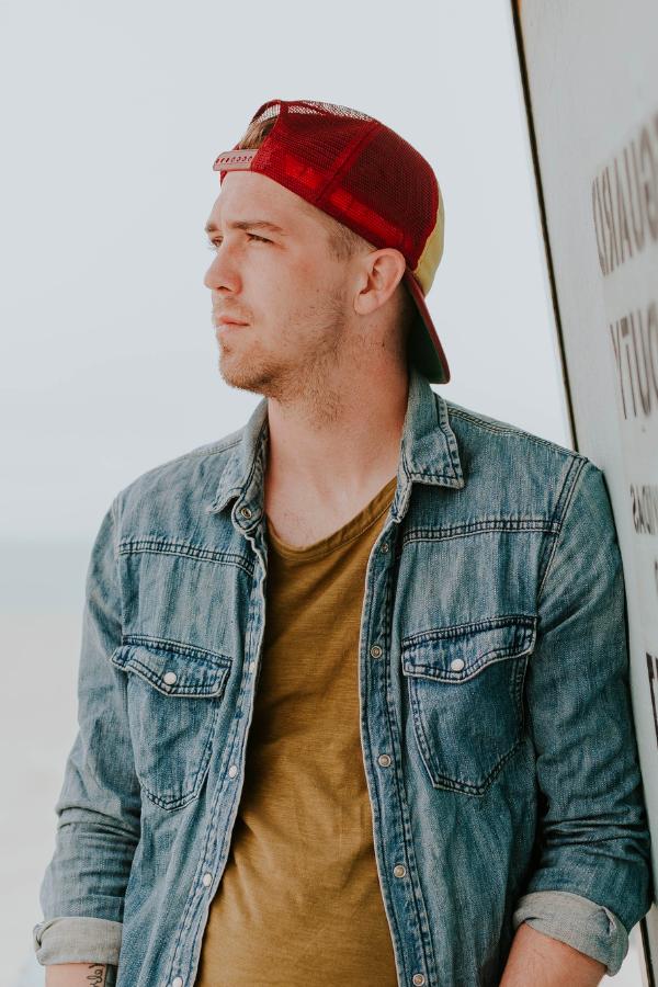 arafed man in a red hat leaning against a surfboard