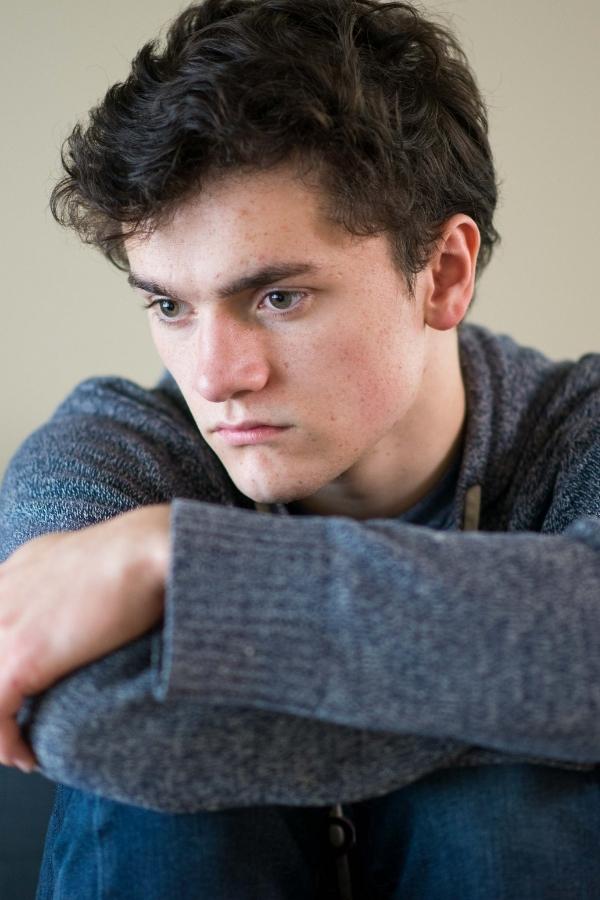 arafed young man sitting on a couch with his arm resting on his knees