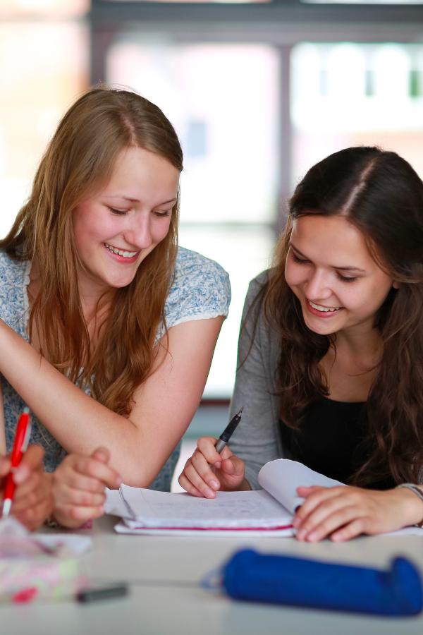 three girls are sitting at a table and smiling while writing