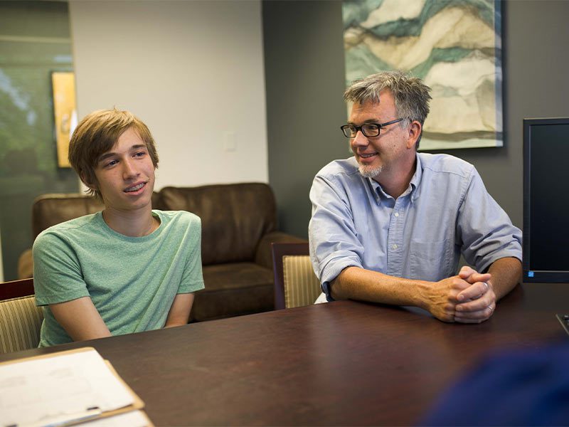 there are two men sitting at a table with a laptop
