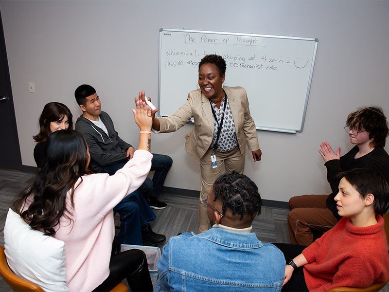 several people sitting in a circle around a white board