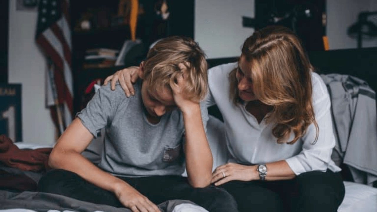 two women sitting on a bed with their hands on their head