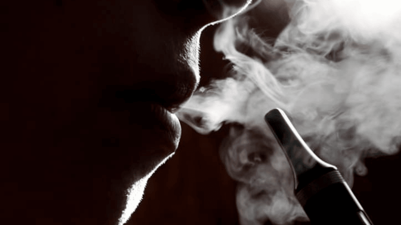 smoke coming out of a person ' s mouth with a cigarette in the background