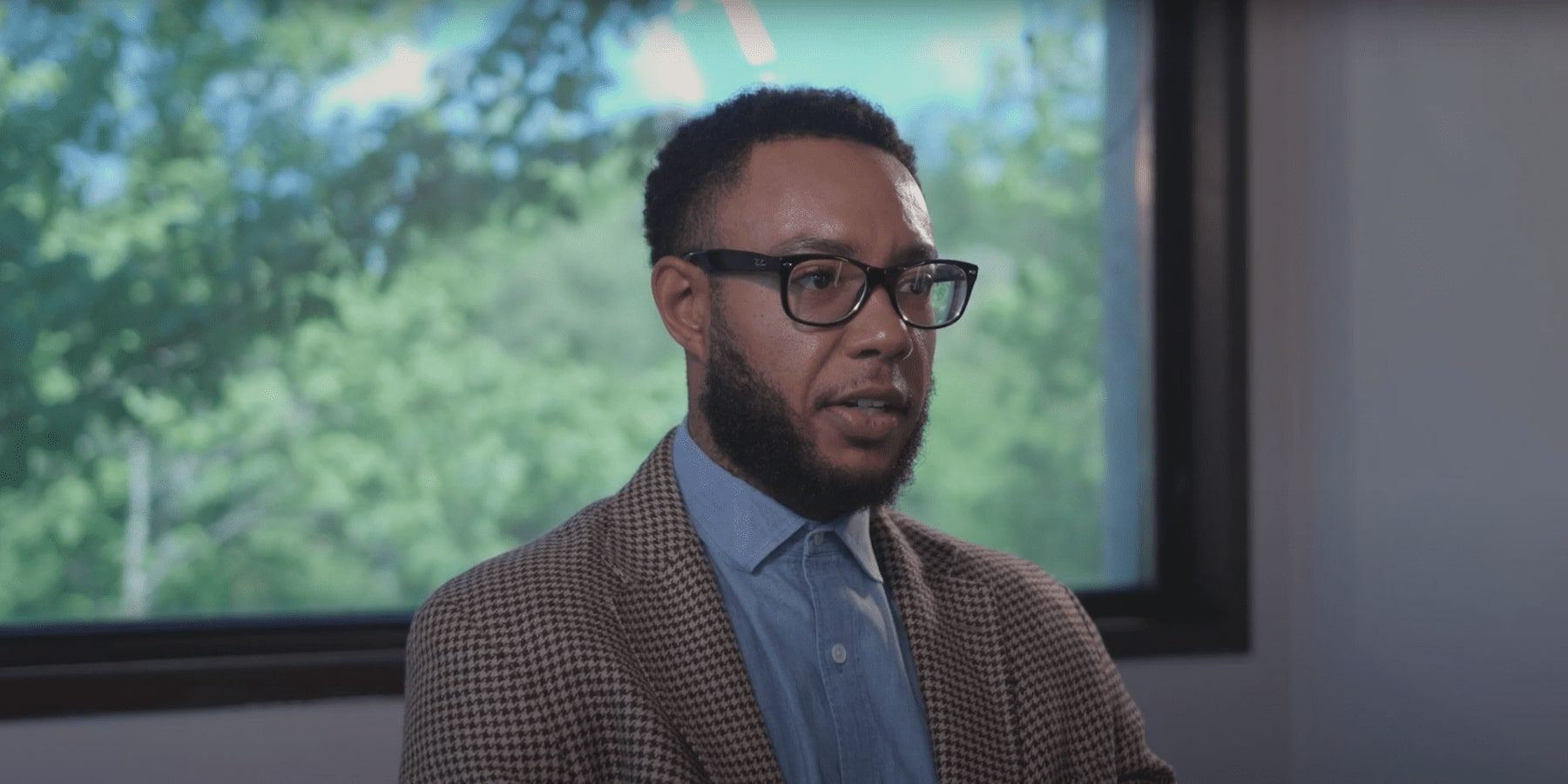 there is a man with glasses and a suit jacket standing in front of a window