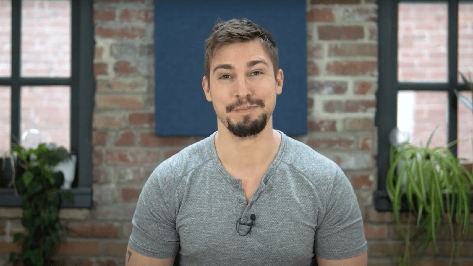 a man in a gray shirt standing in front of a brick wall