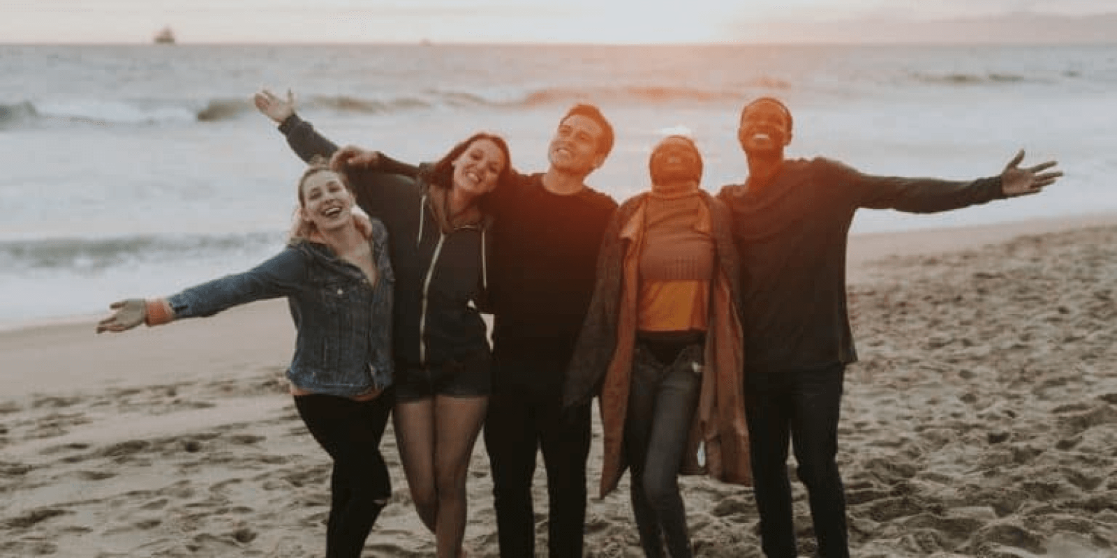 there are four people standing on the beach with their arms outstretched