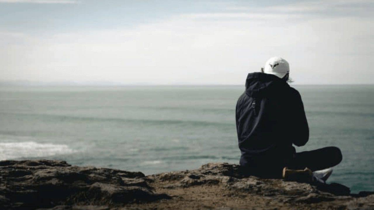 there is a man sitting on a rock looking out at the ocean