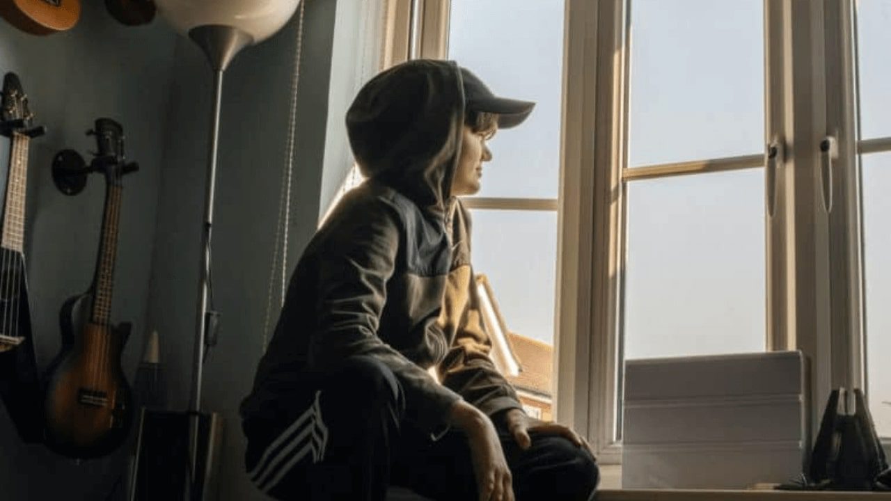 there is a young boy sitting on a window sill looking out