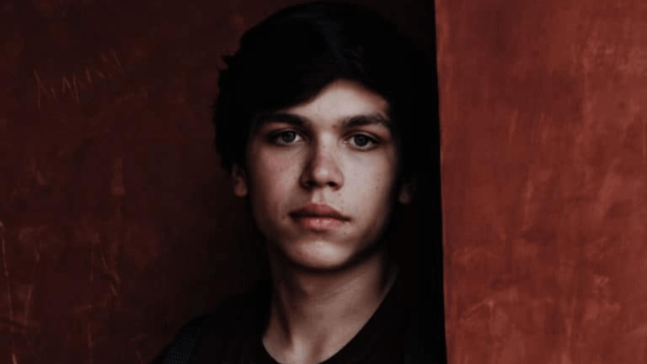 there is a young man standing behind a red wall