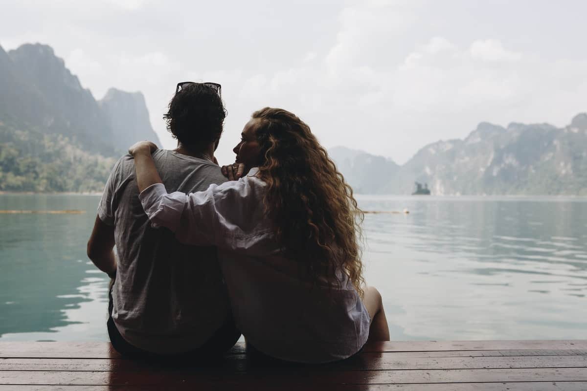 there are two people sitting on a dock looking out at the water