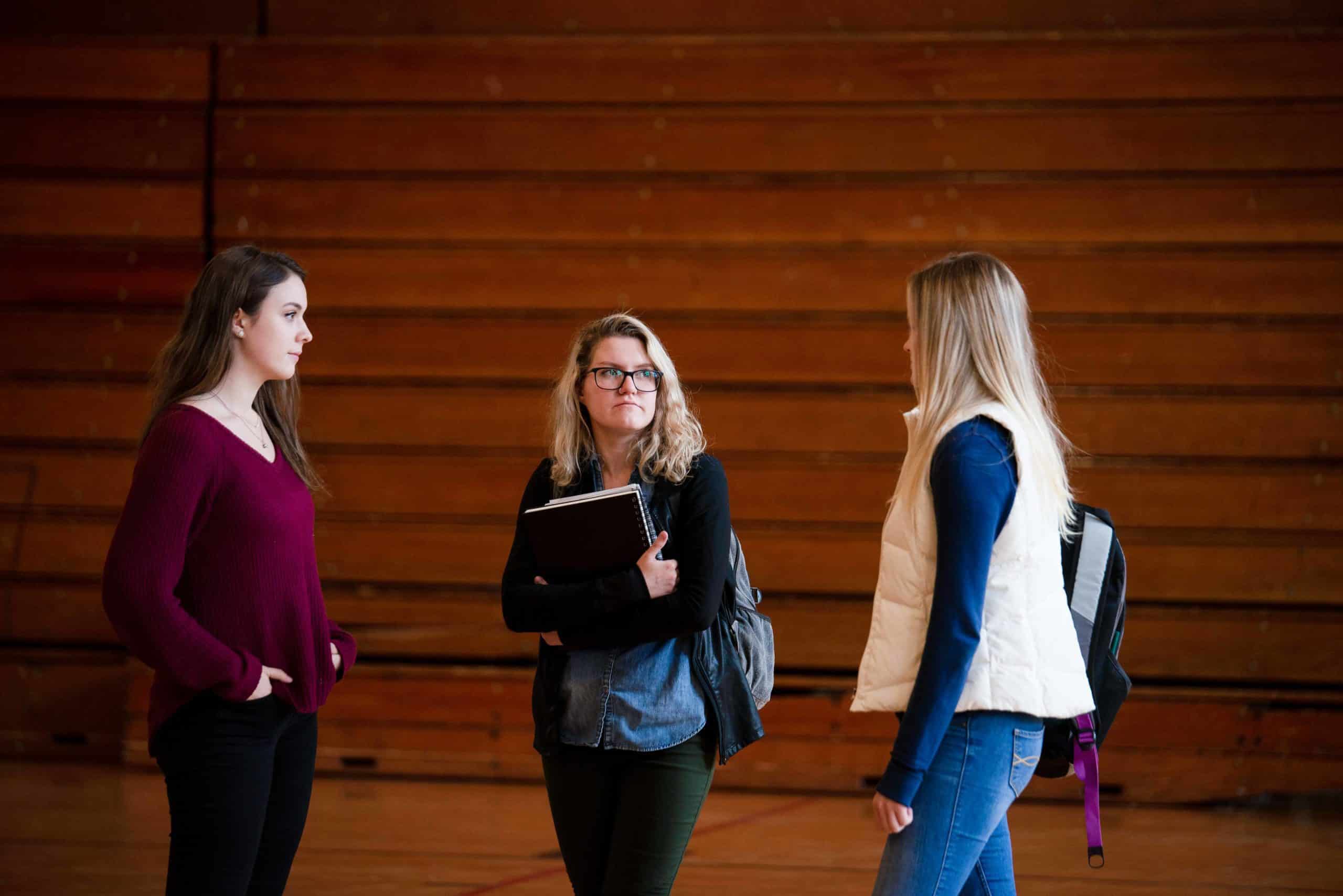 three women standing in a gym with a book in their hands
