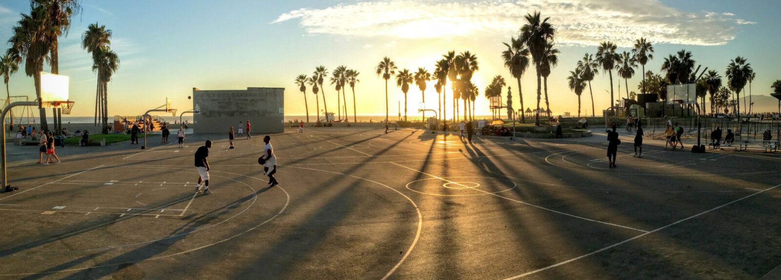 several people playing basketball on a basketball court with palm trees