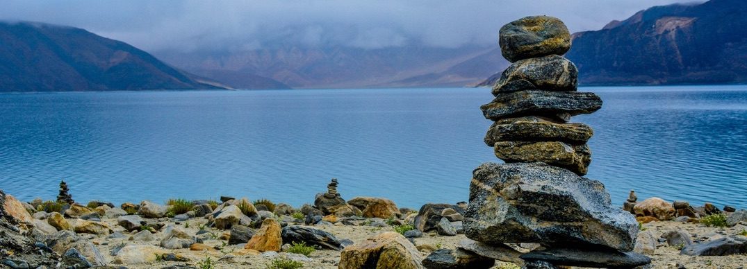 there is a pile of rocks sitting on the shore of a lake
