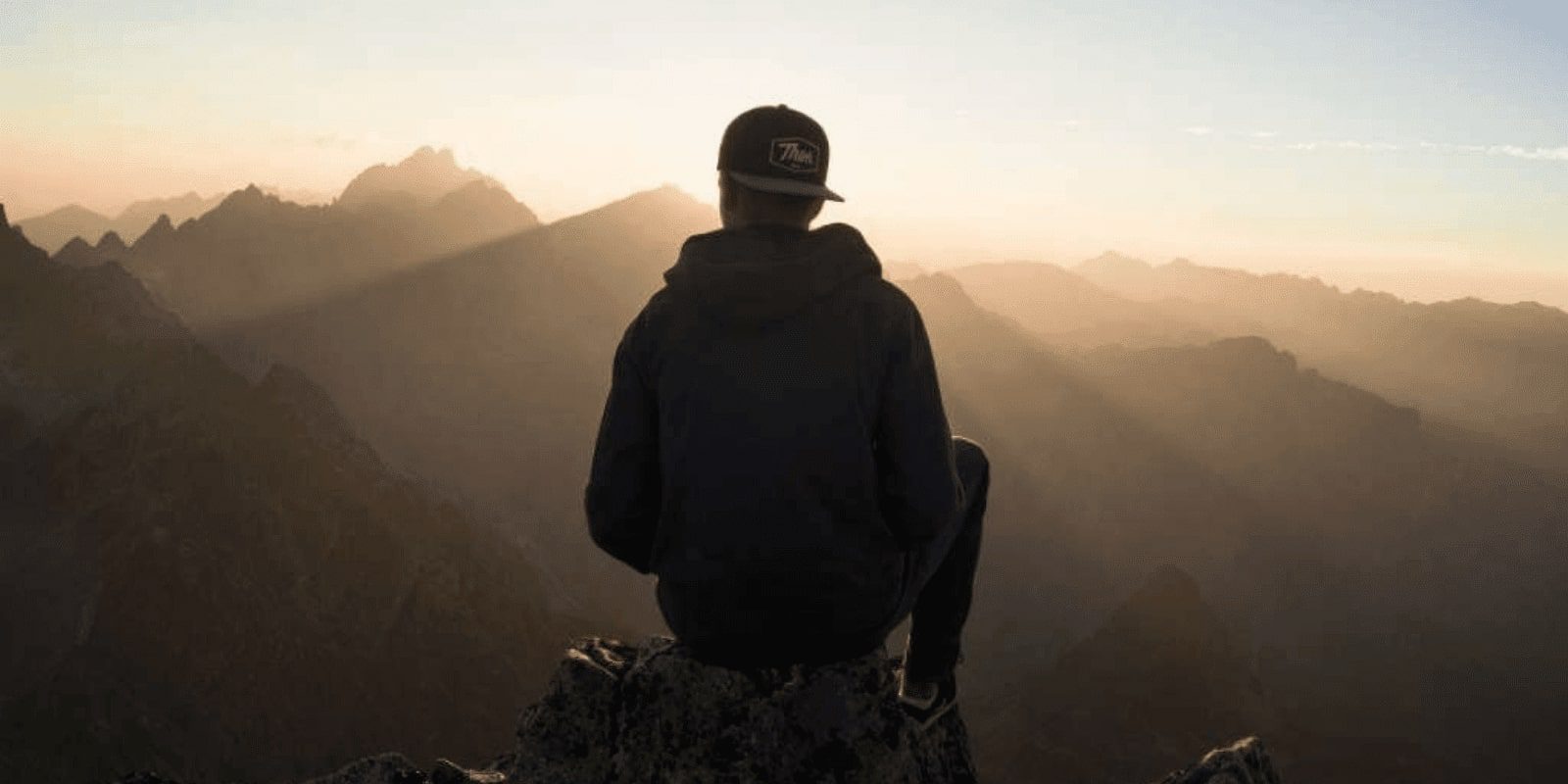 A young man looking at the sunrise in the mountain while sitting on top of the mountain, camera shot from behind